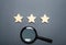 Three stars and a magnifying glass on a dark background. Rating and status of the restaurant or hotel. Prestige. High quality