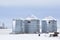 Three steel silos or grain bins covered in snow on a farm in a rural area in winter with a small wagon in the foreground
