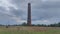 Three storks are standing in a nest built on an old red brick chimney, which is located in the middle of a grass meadow, behind wh