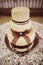 A three-story white wedding cake decorated with a large lace bow of brown