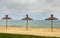 Three straw sunshades on sandy beach.