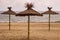 Three straw sunshades on sandy beach.