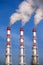 Three striped industrial pipes with smoke over cloudless blue sky