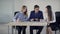 Three students talking sitting on table in classroom.