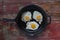 Three sunny side up fried eggs in cast iron pan on wooden table