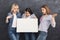 Three surprised girlfriends holding blank white banner