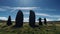 Three Tall People Standing Next To Three Stones With Sky