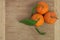 Three tangerines with leaves on wooden board