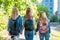 Three teenage girls. They hold each other`s hands. Returns home after school. Summer in nature. Behind backpacks. Back