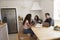 Three teens talk as they study in a kitchen using a computer