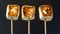 Three Toasted Marshmallows On Sticks With Varying Degrees Of Charring Against A Dark Background