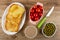 Three toasts in white dish, bowl with tomatoes cherry, knife, jar with meat pate, bowl with green peas on table. Top view