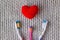 Three toothbrushes and a red heart on a knitted gray background. Two adults, one children`s toothbrush and heart. Love,