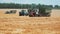 Three tractors with grain bins drive quickly across a field