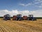 Three tractors harvest straw against a cornfield