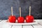 Three traditional red candy apples on a plate against a dark background