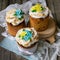 Three traditionally baked orthodox easter cakes with glace icing and bright blue and yellow flowers on woooden