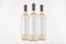 Three transparent wine bottles with blank white labels on white wooden board, mock up.