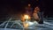 Three travelers by fire right on ice at night. Campground on ice. Tent stands next to fire. Lake Baikal. Nearby there is