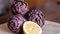 Three Tuscan artichokes and a slice of lemon lit by sunlight on a wooden chopping board