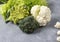 Three types of cabbage on a background of lettuce leaves. Cauliflower, broccoli and cabbage Romanescu Verdone on gray table.