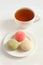 Three types of Japanese dessert mochi - pomegranate with honey, green matcha tea, coconut on a white saucer and a cup of tea