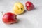 Three ugly red and yellow apples are lying chaotically on grey concrete background