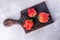 Three ugly ripe red strawberries on burned kitchen cutting board on grey concrete background.