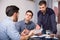 Three upset males with papers at table