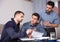 Three upset males with papers at table