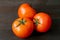 Three vibrant red tomatoes on dark brown wooden table