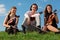 Three violinists sit on grass against sky