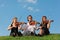 Three violinists sit and play on grass against sky