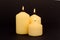 Three wax candles are burning on a black background.