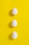 Three white chicken eggs lie on a yellow background