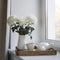 Three white chrysanthemums in a seventies-style fluted vase. Wooden tray with a kettle, milk jug and a cup of tea on the