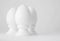 Three white decorative ceramic eggs on stands or in egg-cups on white blurred background. Easter religious Christian symbol. Monoc