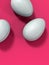 Three white eggs on magenta background, vertical