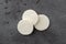 Three white round candy wafers on a gray background illuminated with natural light top view