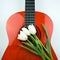 Three white tulips lie on an orange guitar.