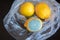 Three whole yellow bright lemons in a cellophane transparent plastic bag. One lemon with light turquoise textured mold,