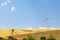 Three wind-driven electric generators against a yellow field and blue sky. Summer sunny day