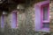Three windows pink violet of a house made of stones and bricks