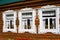 Three windows of a wooden county house decorated by white frames