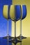 Three wineglasses on a shiny surface with water that distort yellow and blue background