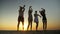 Three women and a man dancing on a beach at twilight