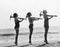 Three women posing with a pick ax on the beach