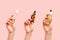 Three women& x27;s hands hold glass multi-colored bottles with oil and serum. Pink background, close-up. The concept of