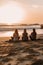 Three women sitting on the beach watching the sun set. AI generative image.