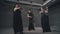 Three women violinists in beautiful black dresses playing instruments in a gray concrete room.